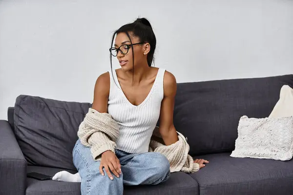 A young, beautiful woman sits on a couch, absorbed in her studies from home in a relaxed setting. — Stock Photo