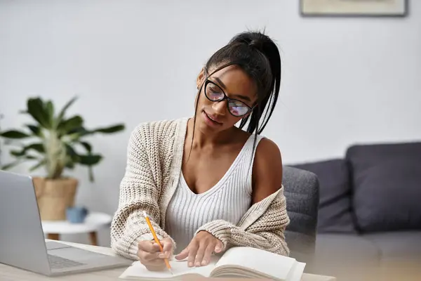 In a cozy home setting, a young woman focuses on her studies, jotting notes in her notebook. — Stock Photo
