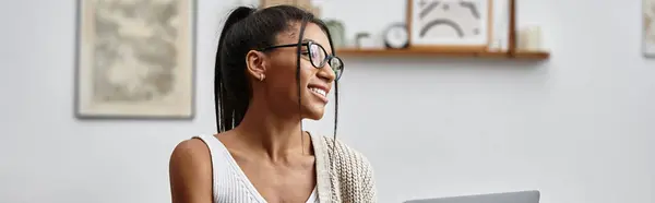 A young woman enjoys studying from home, smiling as she engages with her laptop and materials. — Stock Photo