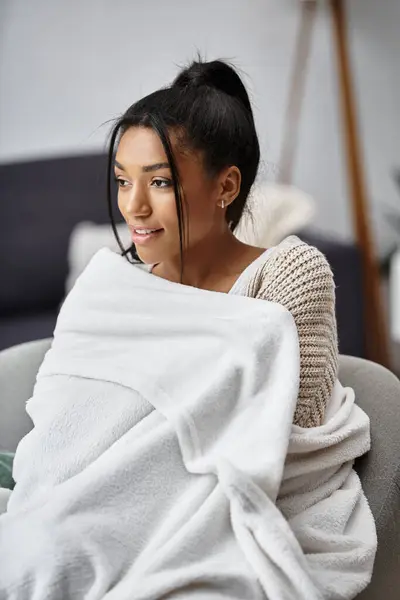 A beautiful young woman studies intently from her home dressed comfortably in a warm blanket. — Stock Photo