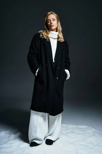 Une jeune femme confiante se tient gracieusement dans un manteau noir chic et un pull blanc élégant. — Photo de stock