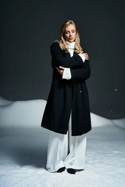 Una bella giovane donna si erge con grazia in un cappotto nero, trasudando eleganza in mezzo alla neve soffice. — Stock Photo