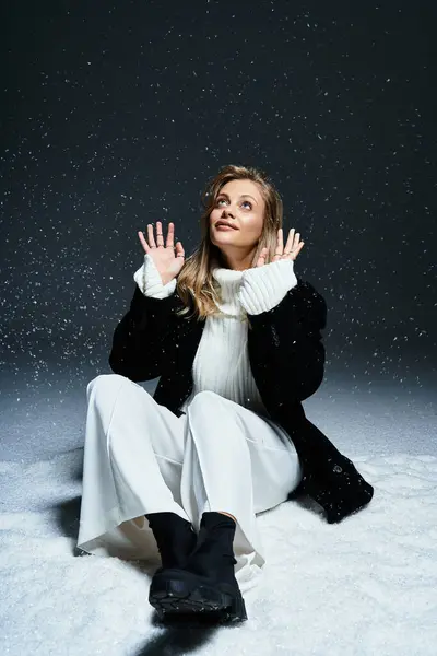 A beautiful young woman sits in fresh snow, delighting in the gentle snowfall around her. — Stock Photo