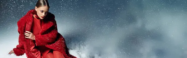 A young beautiful woman elegantly poses amid swirling snowflakes, showcasing her stylish red attire. — Stock Photo