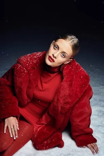 A young woman wearing a vibrant red ensemble relaxes against a snowy backdrop, radiating elegance. — Stock Photo