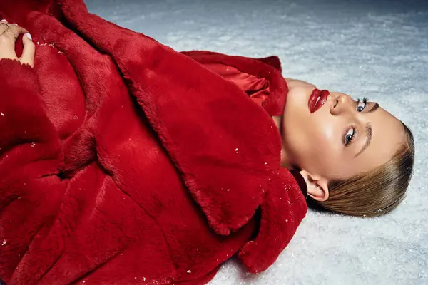 A young woman in a red coat lies elegantly on snow against a serene winter backdrop. — Stock Photo