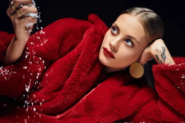 A young woman elegantly dressed in red relaxes while gracefully scattering snow. — Stock Photo
