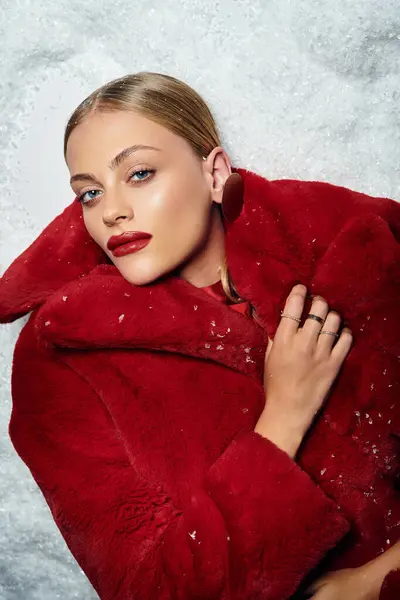 Una bella giovane donna si rilassa con grazia in un suggestivo cappotto rosso, circondata da una soffice neve. — Foto stock