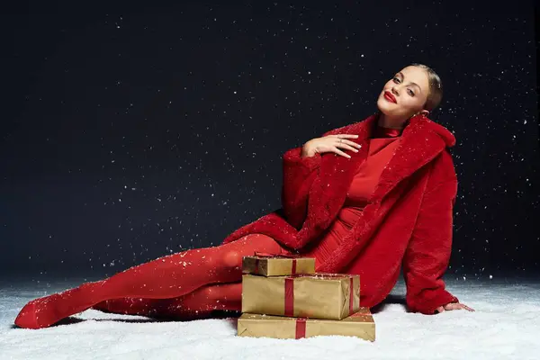 Una bella donna si rilassa in un lussuoso vestito rosso con regali intorno a lei in un'atmosfera invernale. — Foto stock