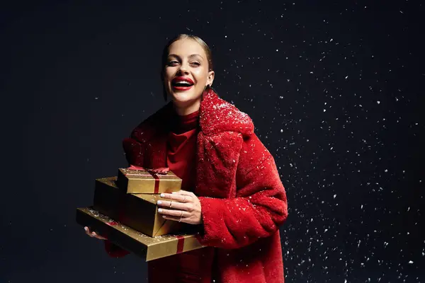 A cheerful young woman enjoys a snowy atmosphere while holding holiday presents, radiating joy. — Stockfoto