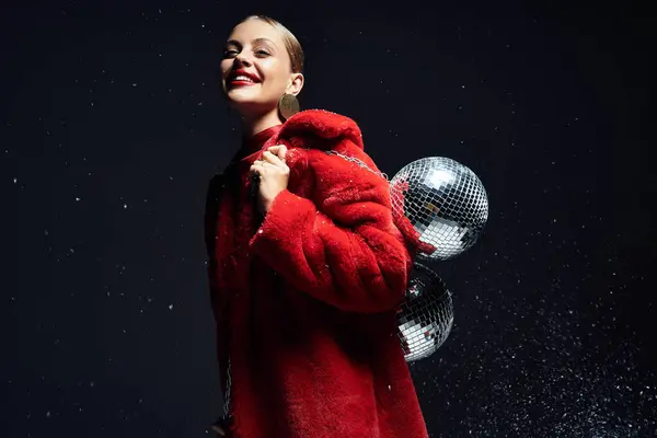 The young woman smiles brightly while showcasing her festive red coat and shimmering disco balls. — Stock Photo