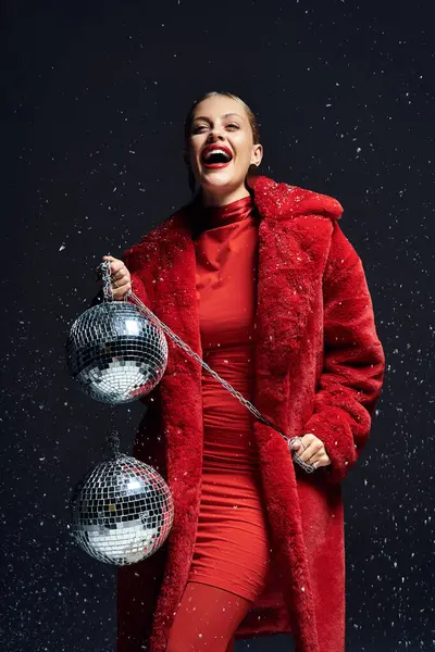 A young woman in festive red holds sparkling disco balls, embracing winter spirit. — Stock Photo