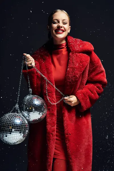 A young woman in a bright red coat beams happily while holding disco balls. — Stock Photo