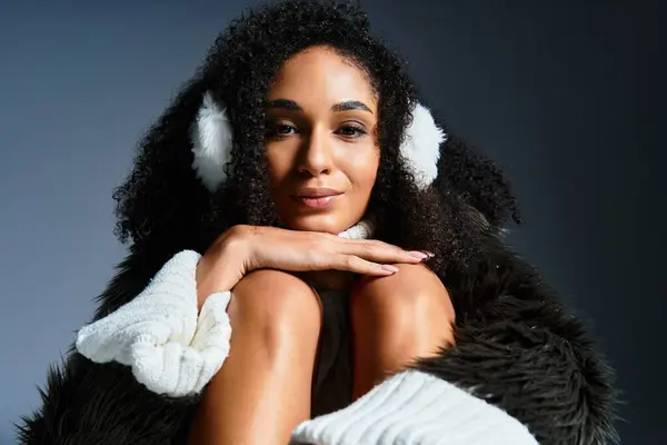 Una bella donna bruna indossa paraorecchie e una giacca di pelliccia sintetica, trasudando vibrazioni della moda invernale in uno studio. — Foto stock
