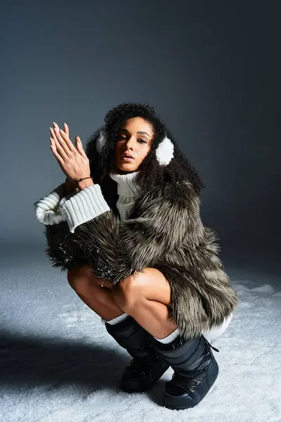 A fashionable brunette showcases winter attire with earmuffs and a faux fur jacket in a sleek studio environment. — Stock Photo