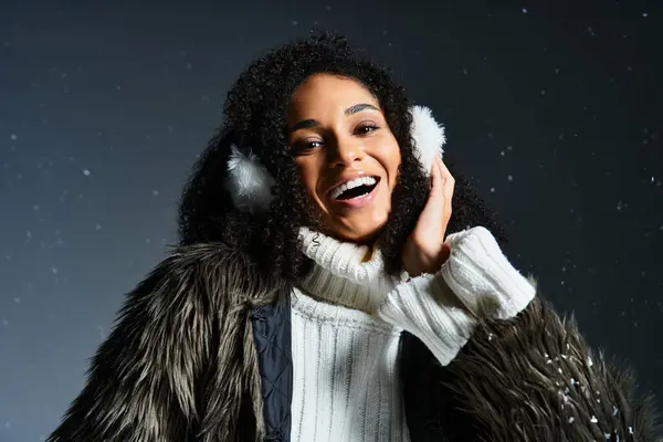 Una donna afroamericana elegante sorride brillantemente mentre mostra la moda invernale con paraorecchie e un maglione caldo. — Foto stock
