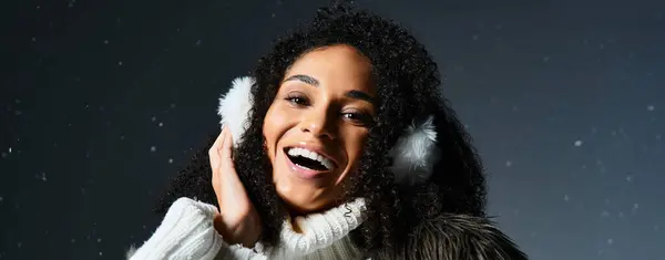 Una donna bruna allegra ed elegante con i paraorecchie e una giacca di pelliccia sorride calorosamente in uno studio a tema invernale. — Foto stock