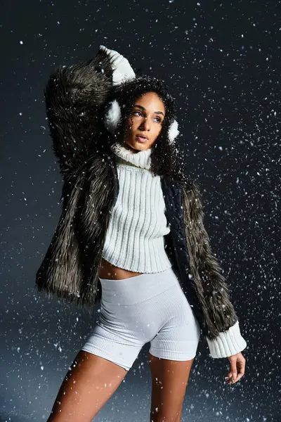 Una donna bruna alla moda modella un outfit invernale chic, completo di paraorecchie ed eco-pelliccia, tra la neve che cade. — Foto stock