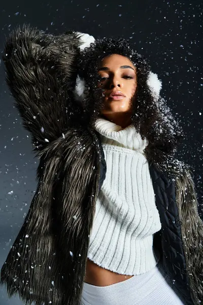Una bella donna afroamericana in paraorecchie e una giacca di pelliccia ecologica irradia eleganza invernale in uno studio. — Foto stock