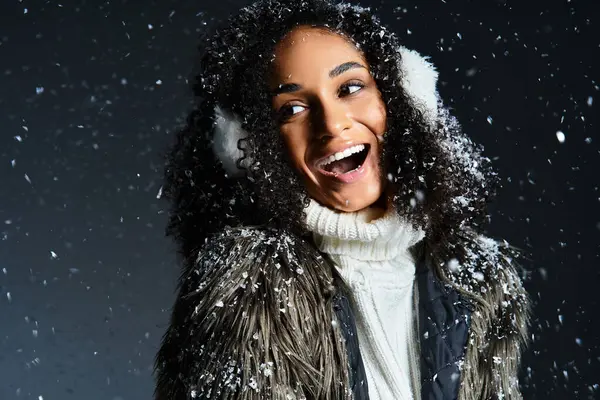 Una bella donna bruna in paraorecchie e pelliccia sintetica mostra calorosamente la sua moda invernale in uno studio. — Foto stock