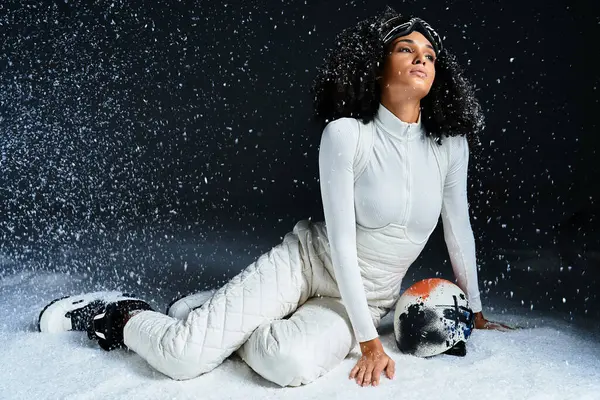 A fashionable brunette woman in a ski suit poses gracefully in a snowy studio setting. — Stock Photo