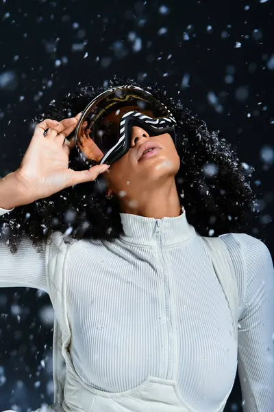 A beautiful brunette woman models a chic ski suit, exuding winter fashion elegance in a snowy studio setting. — Stock Photo