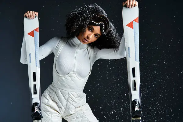 A beautiful African American woman in a ski suit poses confidently with skis, embodying winter chic in a studio. — Stock Photo