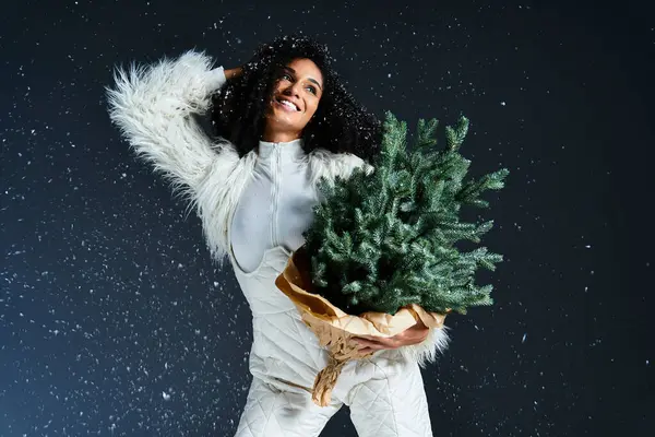A beautiful woman embraces winter magic while joyfully holding a small Christmas tree, dressed elegantly. — Stock Photo