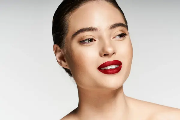 Una mujer impresionante con lápiz labial rojo vibrante expresa confianza y estilo en la iluminación suave. - foto de stock