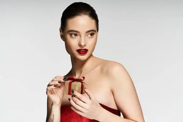 In a graceful pose, a woman with a captivating expression holds a small gift, radiating elegance. — Stock Photo