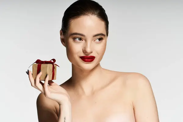 Uma mulher deslumbrante detém um pequeno presente com uma expressão lúdica em um cenário limpo. — Fotografia de Stock