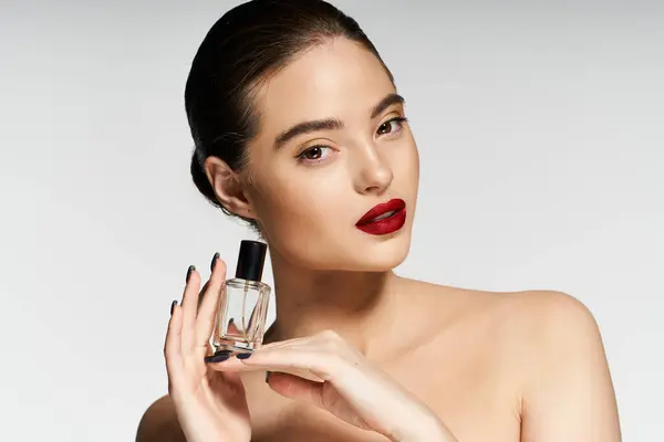 Confident woman holds a nail polish bottle while highlighting her vibrant red lips and beauty. — Stock Photo