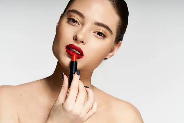 The woman expertly applies bright red lipstick, accentuating her natural beauty and elegance. — Stock Photo