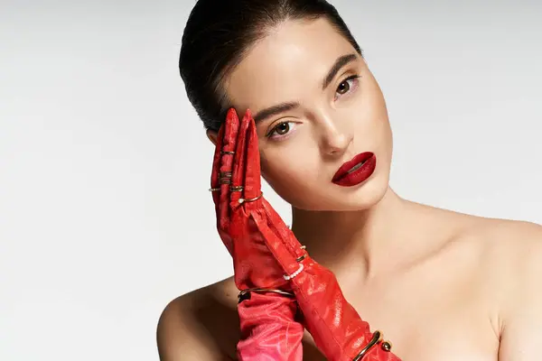 A beautiful woman with striking features showcases her artistic pose while wearing bold red gloves. — Stock Photo