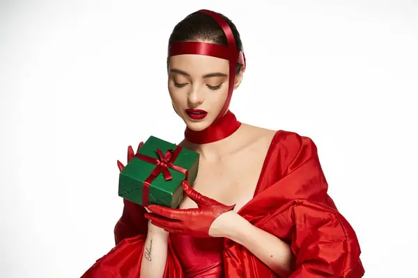 Elegant figure dressed in striking red, gently cradling a beautifully wrapped present. — Stock Photo
