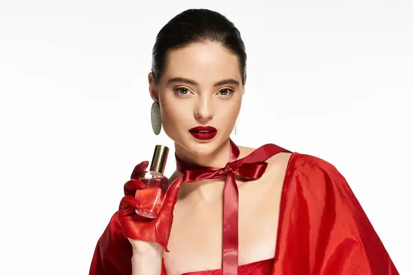 A stunning woman in striking red attire highlights a perfume in her graceful hand. — Stock Photo