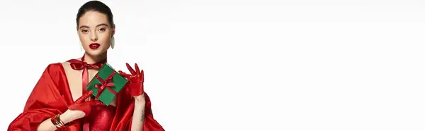 A stylish woman dons vibrant red, holding a green gift adorned with a bow, radiating joy. — Stock Photo