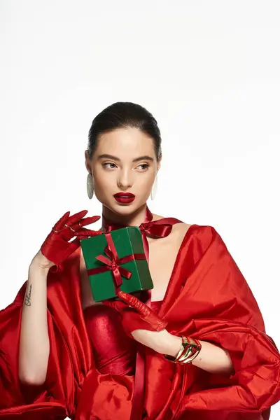 The elegant woman dressed in vibrant red showcases a small green gift box during a joyful event. — Stock Photo