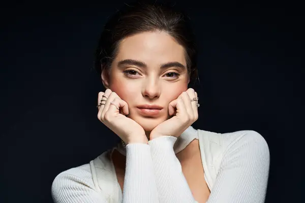 La donna guarda pensieroso, elegantemente incorniciando il viso con le mani gentili in luce soffusa. — Foto stock