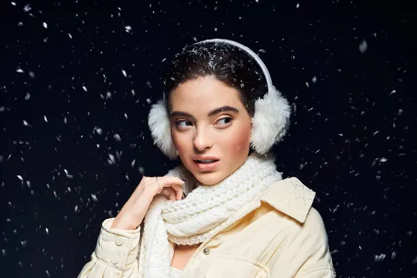 Una mujer elegante se encuentra en medio de copos de nieve, adornada con un cálido equipo de invierno, expresando serenidad. - foto de stock