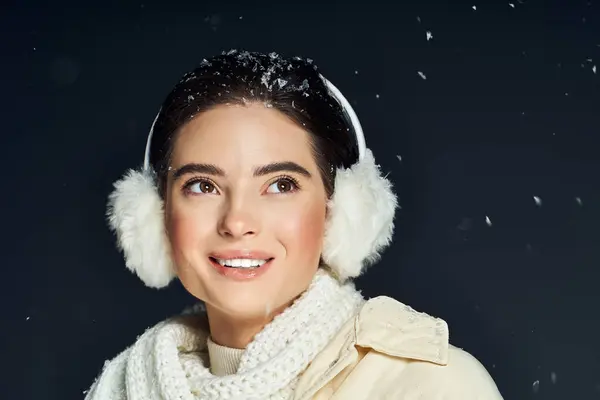 A cheerful woman with earmuffs smiles warmly as snowflakes gently fall around her. — Stock Photo