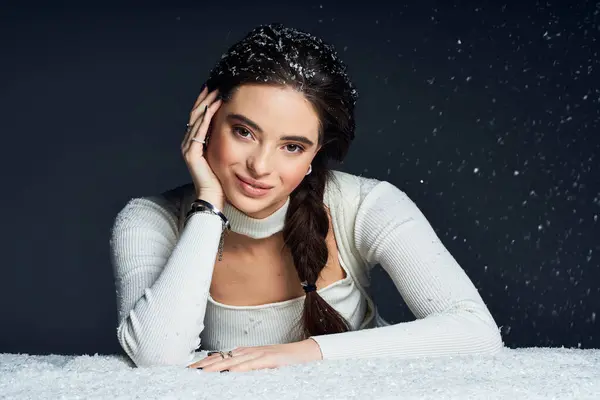 The elegant woman rests her chin on her hand, illuminated by soft light amidst swirling snow. — Stock Photo