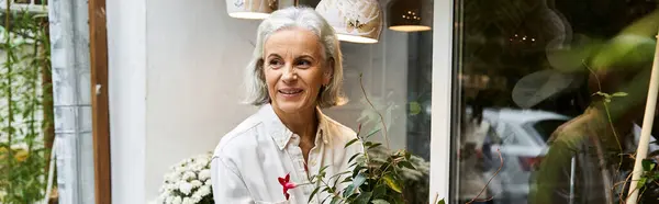 A joyful mature woman is nurturing greenery while surrounded by beautiful floral accents. — Stock Photo