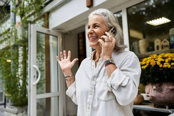 A delighted woman speaks on the phone while surrounded by vibrant flowers and greenery. — Stock Photo