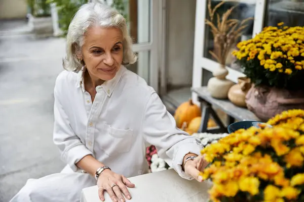 A mature woman enjoys the beauty of blooming flowers, embracing tranquility in nature. — Stock Photo
