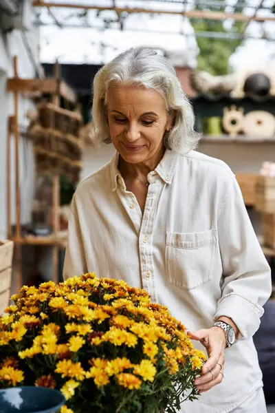 A beautiful mature woman carefully tends to a bouquet of cheerful yellow flowers in a garden shop. — Stock Photo
