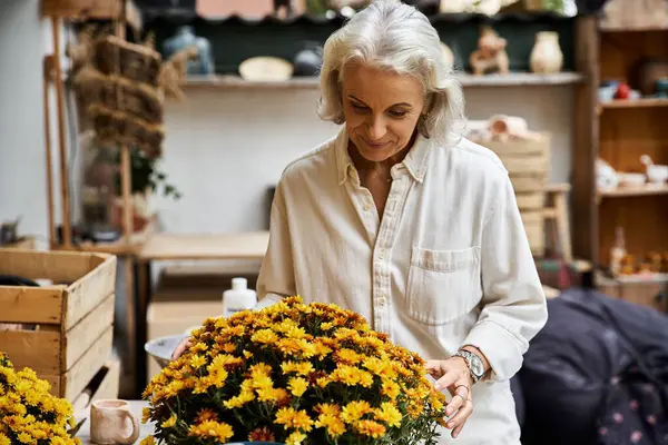 A beautiful mature woman carefully arranges bright flowers in a cozy artisan workshop. — Stock Photo