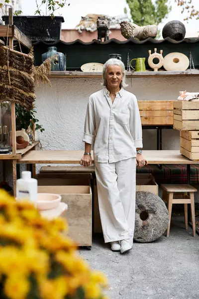 An elegant mature woman stands gracefully in a lively workshop filled with artistic treasures. — Stock Photo