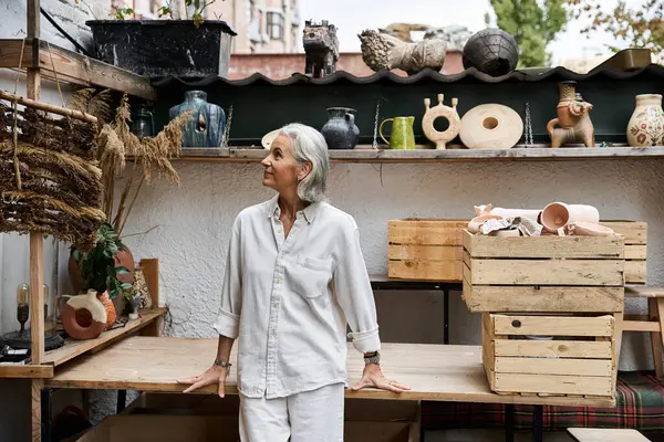 Eine schöne reife Frau bewundert handgefertigte Keramik und Dekor in einer einzigartigen Werkstatt-Umgebung. — Stockfoto