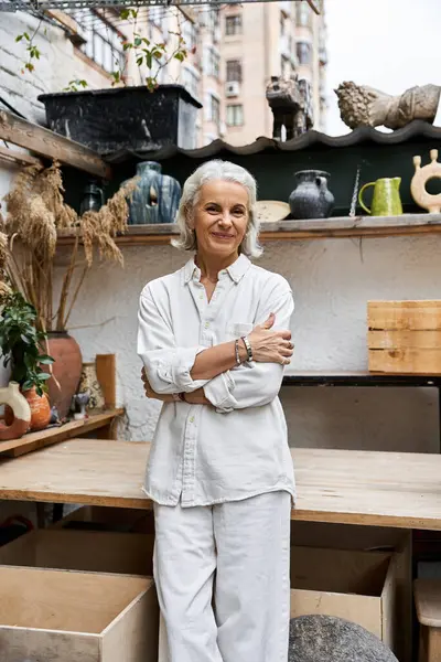 A graceful mature woman poses in her artistic studio filled with unique decorations and plants. — Stock Photo